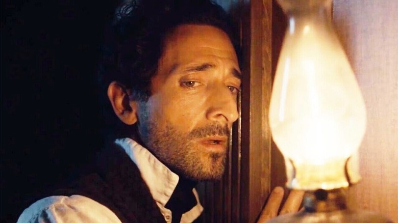 Charles Boone (Adrien Brody) listens to a wooden wall next to a gas lamp in Chapelwaite