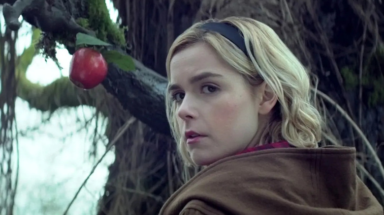 Sabrina Spellman (Kiernan Shipka) looks back from a red apple growing from a gnarled tree in Chilling Adventures of Sabrina