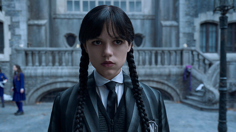 Wednesday Addams (Jenna Ortega) stands inquisitively in the courtyard of a school in Wednesday