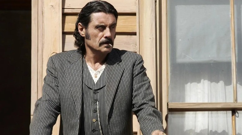 Al Swearengen (Ian McShane) stands sternly on a balcony with a toothpick in his mouth on Deadwood