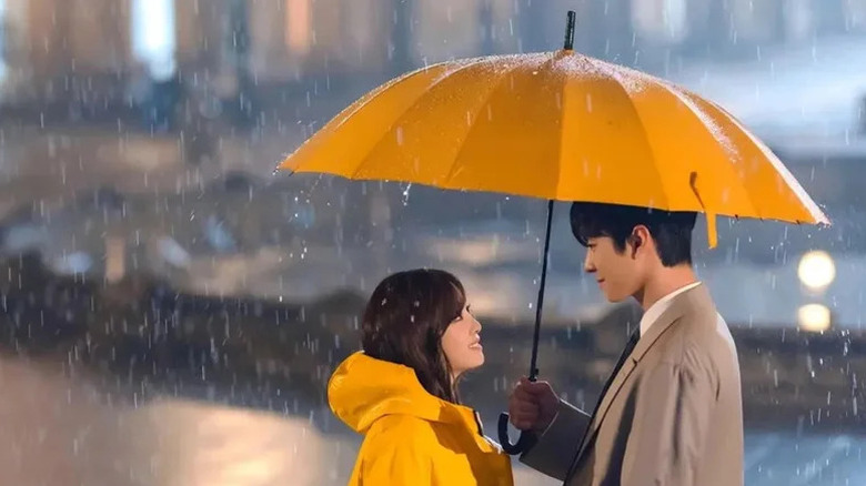 Kang Tae-moo (Ahn Hyo-seop) holds a yellow umbrella over Shin Ha-ri (Kim Se-jeong) in the pouring rain in Business Proposal