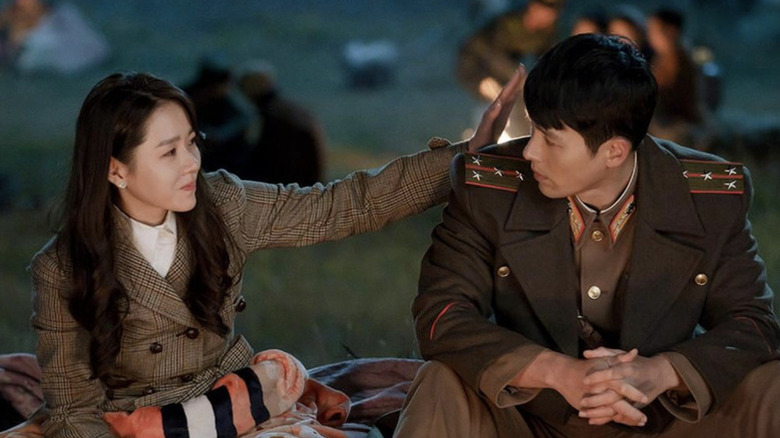 Yoon Se-ri (Son Ye-jin) reaches out to touch Ri Jeong-hyeok (Hyun Bin) by a campfire in Crash Landing on You