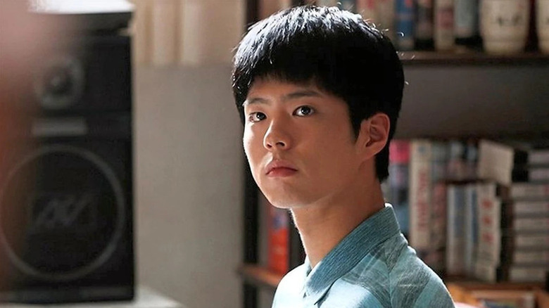 Choi Taek (Park Bo-gum) sits by a speaker and bookcase in Reply 1988