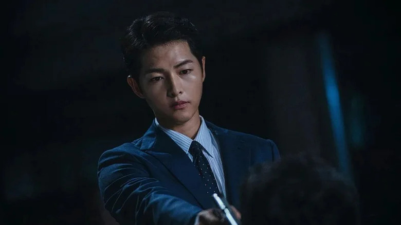 Vincenzo Cassano (Song Joong-ki) aims a pistol at someone kneeling before him in Vincenzo