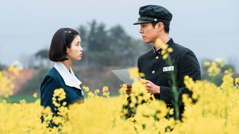 Oh Ae-sun (IU) looks at Yang Gwan-sik (Park Bo-gum) holding a letter in a flowering field in When Life Gives You Tangerines