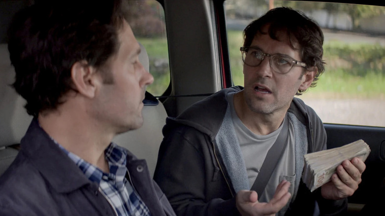 Paul Rudd as Clone Miles sitting in a car next to Original Miles wearing glasses and holding a wad of cash in Living With Yourself