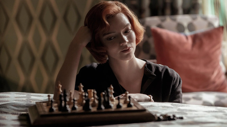 Anya Taylor-Joy as Beth Harmon smiling while looking at a chess set in The Queen's Gambit