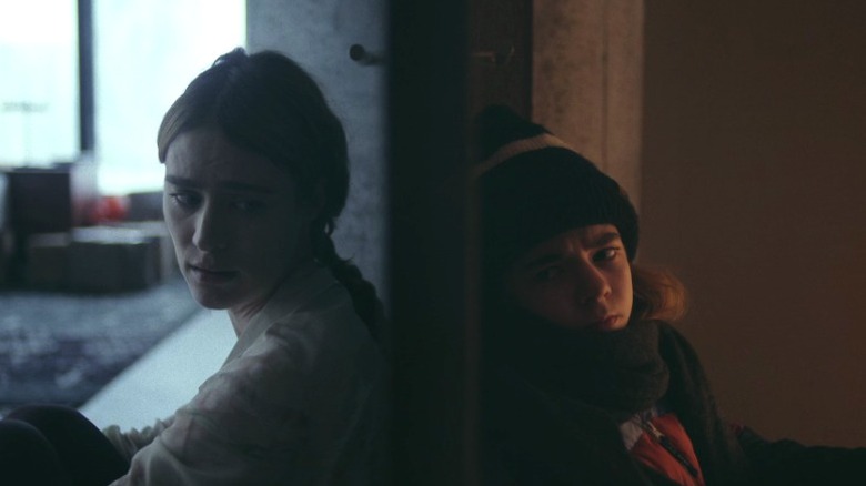 Older (Mackenzie Davis) and younger Kirsten Raymonde (Matilda Lawler) sitting on opposite sides of a wall on Station Eleven S1E7