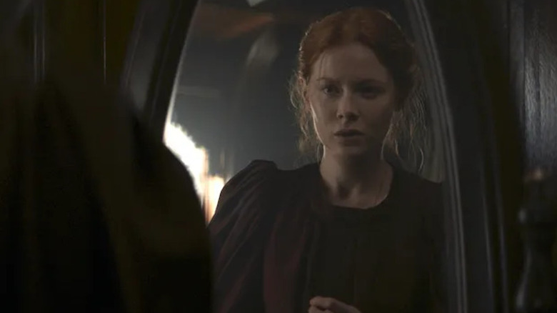 Maura Henriette Franklin (Emily Beecham) stands in a doorway expectantly in 1899