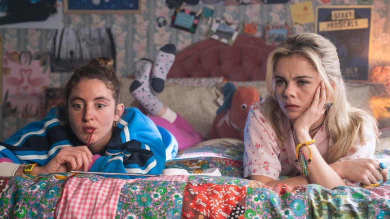 Saoirse-Monica Jackson and Louisa Harland as Erin and Orla, sitting on a bed together in Derry Girls.