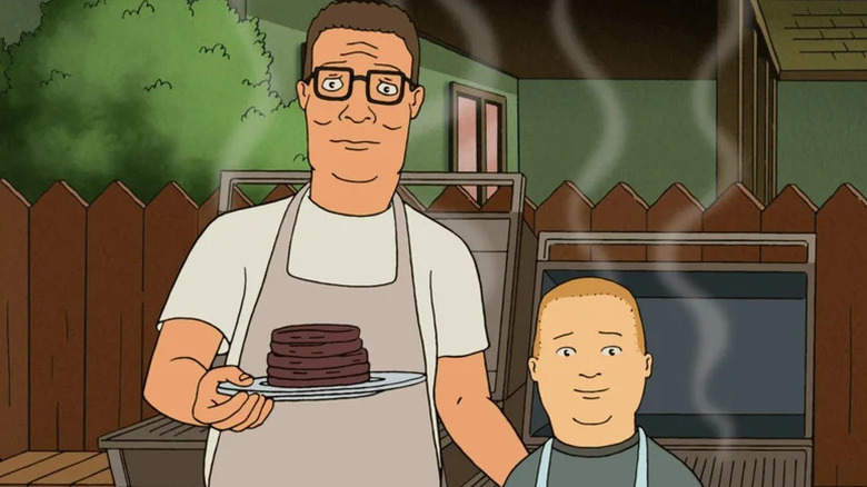 Animated Hank Hill holding burgers in front of a grill with his son Bobby in King of the Hill