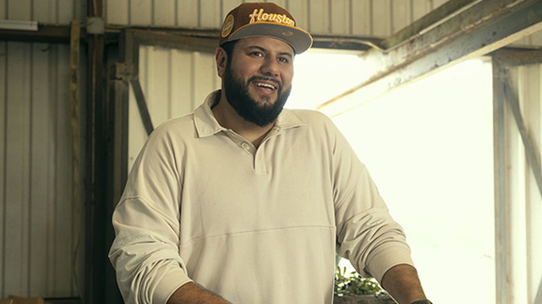 Mo Amer smiling in a baseball cap in Mo