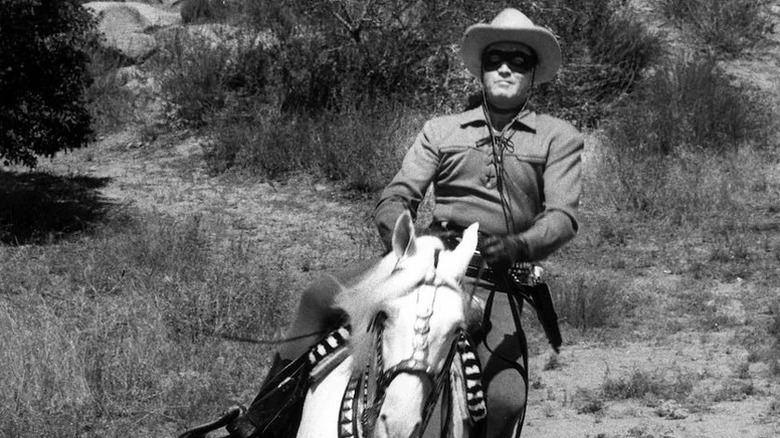 Clayto Moore as The Lone Ranger wearing a black mask and hat riding a horse in The Lone Ranger