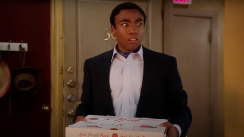 Donald Glover as Troy, reentering an apartment with pizza on Community.