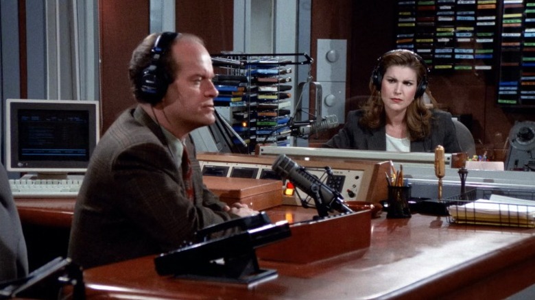 Frasier Crane hosting his radio show while Roz Doyle watches from outside the booth on S3E15