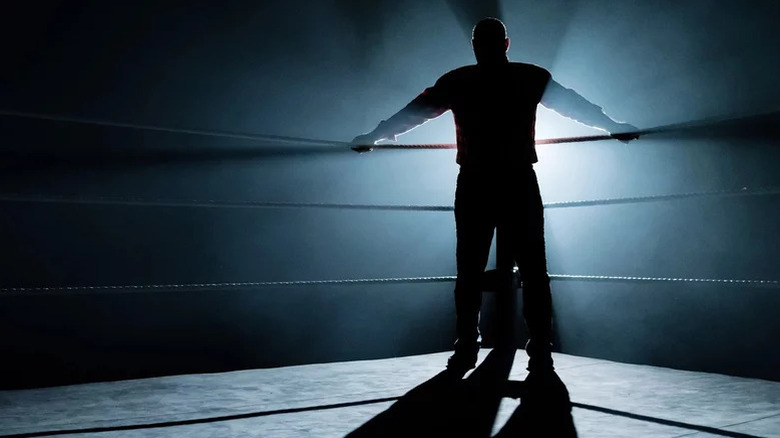 A wrestler grabs the turnbuckle inside a darkened wrestling ring on Dark Side of the Ring