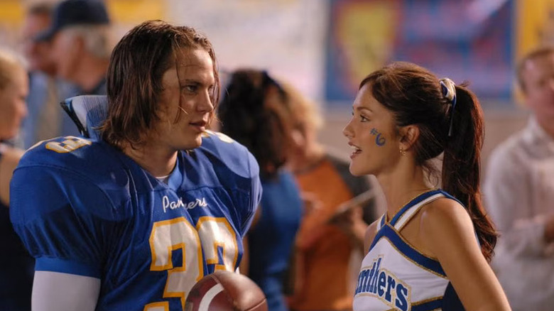 Tim Riggins (Taylor Kitsch) in his football uniform stands next to Lyla Garrity (Minka Kelly) in her cheerleader outfit on Friday Night Lights