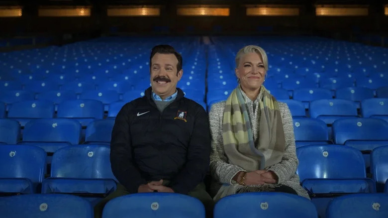 Ted Lasso (Jason Sudeikis) sits smiling next to Rebecca Welton (Hannah Waddingham) in an empty stadium on Ted Lasso