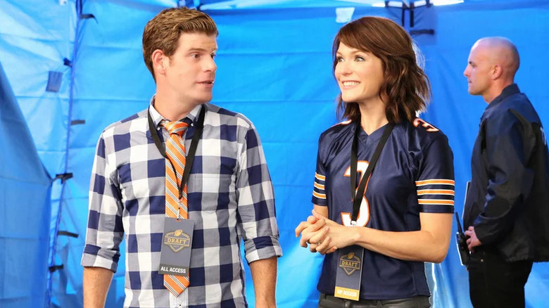 Kevin MacArthur (Stephen Rannazzisi) looks at a smiling Jenny MacArthur (Katie Aselton) wearing NFL All-Access passes on The League