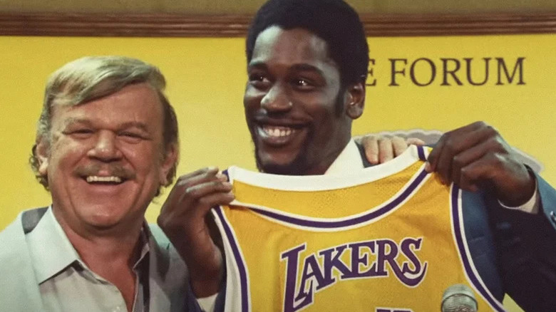Jerry Buss (John C. Reilly) smiles next to a grinning Magic Johnson (Quincy Isaiah) holding a Los Angeles Laker jersey on Winning Time: The Rise of the Lakers Dynasty