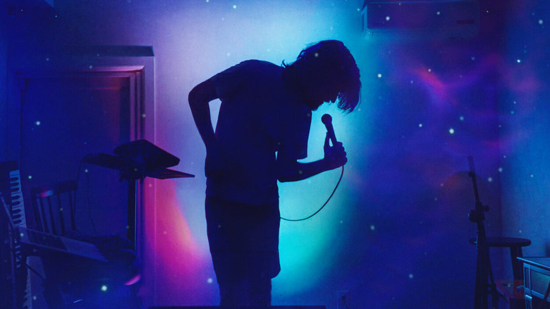 Bo Burnham holds a microphone while looking down in a psychedelic room in Bo Burnham: Inside (2021)