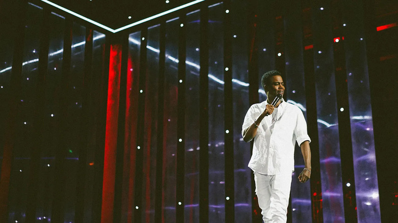 Chris Rock walks across a stage while speaking into a microphone in Chris Rock: Selective Outrage (2023)
