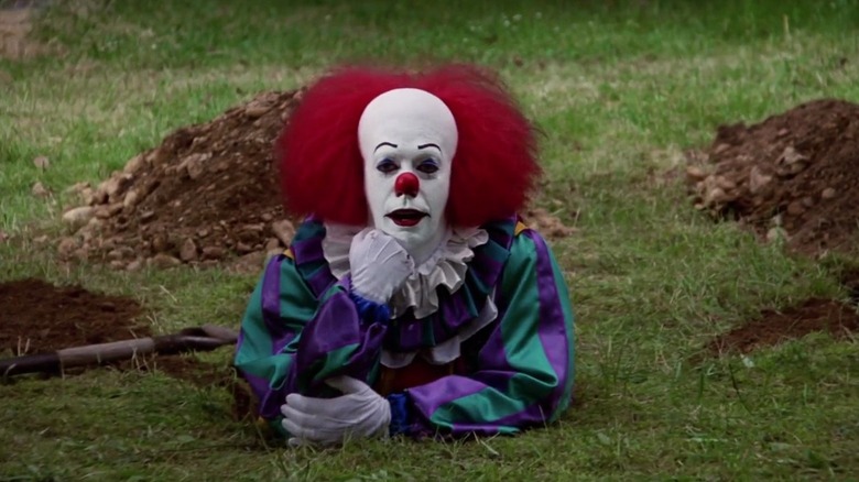 Tim Curry as Pennywise sits in a hole in IT