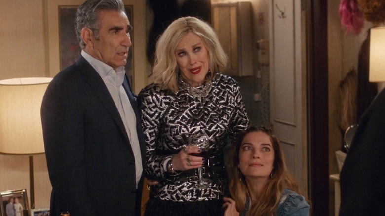 Catherine O'Hara as Moira Rose holding a glass of wine next to Eugene Levy as Johnny and hugging Annie Murphy as Alexis
