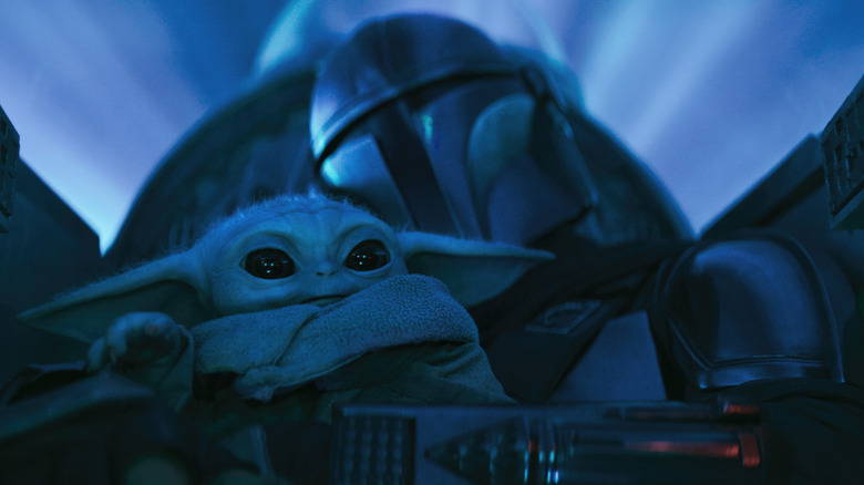 Din Djarin flying a ship while holding Grogu in The Mandalorian