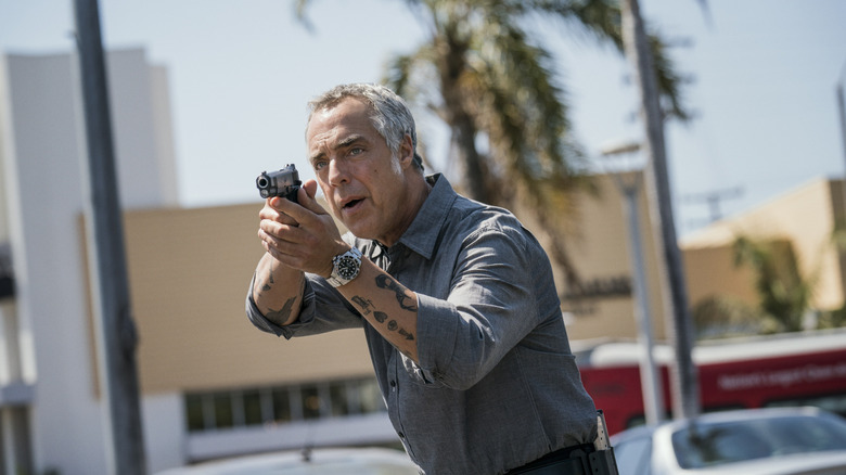 Titus Welliver as Harry Bosch pointing gun with tattoos on forearms and palm tree behind him in Bosch