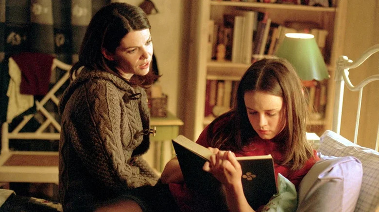 Lauren Graham as Lorelai sitting on bed next to Alexis Bledel as Rory reading a book in Gilmore Girls