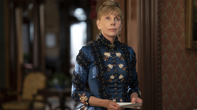 Christine Baranski in 19th century blue dress with hair up holding piece of paper in The Gilded Age