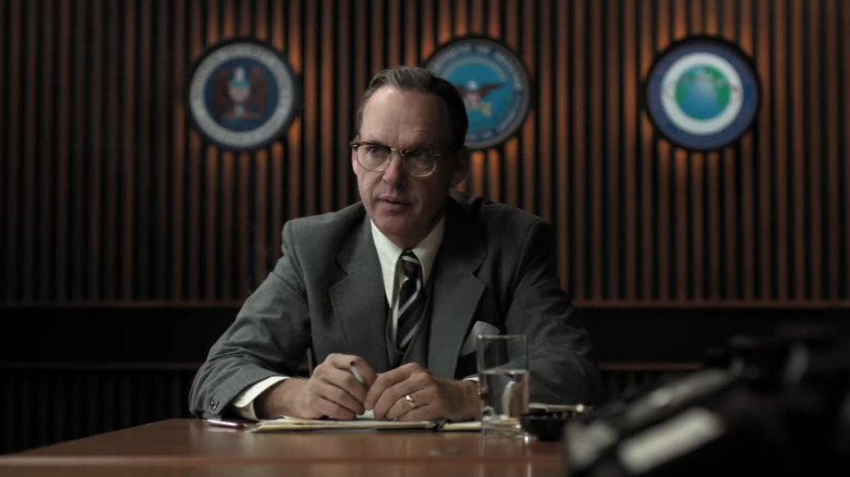 Michael Keaton's James Jesus Angleton sitting at a table and wearing a suit on The Company