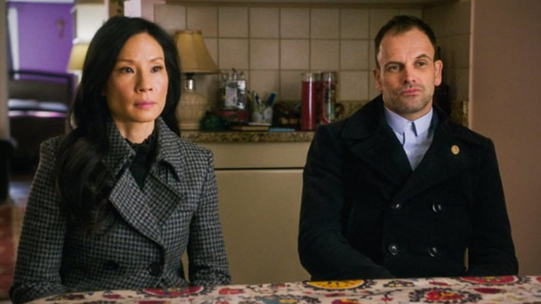 Lucy Liu as Joan Watson sitting next to Jonny Lee Miller as Sherlock Holmes in Elementary