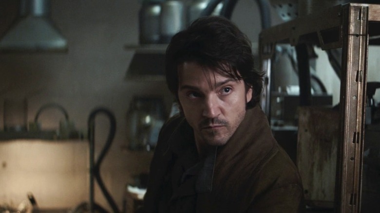 Cassian standing by a metal rack and looking to his left on Andor S1E12