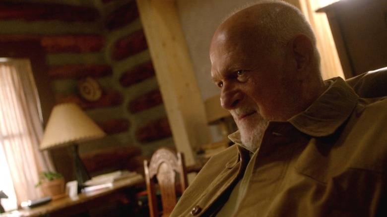 Barlow sitting in a chair and smiling wickedly on Longmire S4E3