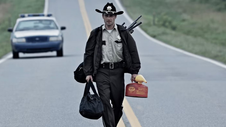 Andrew Lincoln as Rick Grimes, walking down a road with equipment in The Walking Dead.