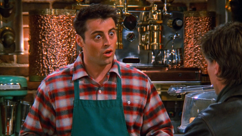 Matt LeBlanc as Joey Tribbiani wearing an apron and working at Central Perk while taking to a customer in Friends