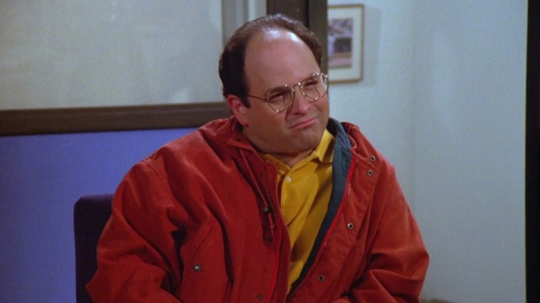 George sitting in a chair and smirking on Seinfeld S5E22