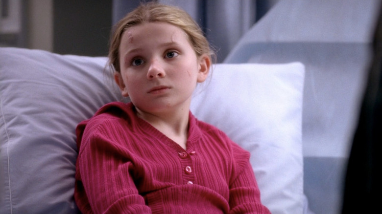 Megan Clover in pink sweater in hospital bed, looking on