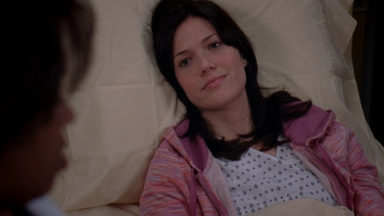 Mary Portman in hospital gown and pink jacket, laying on bed and smiling