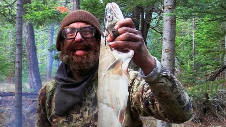 Bearded man smiling and holding up fish on Alone