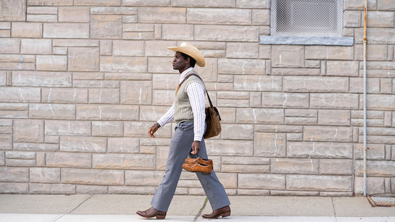 Conphidance as Iwegbuna Ikeji walking dow the street wearing cowboy hat and boots in Little America