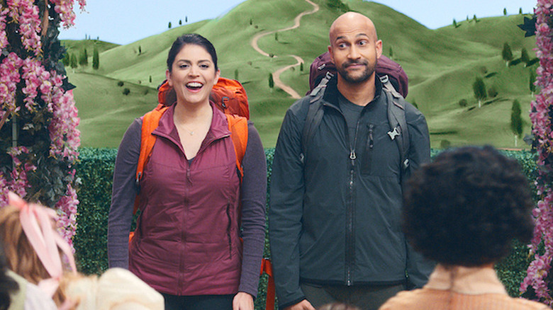 Cecily Strong as Melissa and Keegan-Michael Key as Josh wearing backpacks and standing in front of painted backdrop of hills in Schmigadoon!