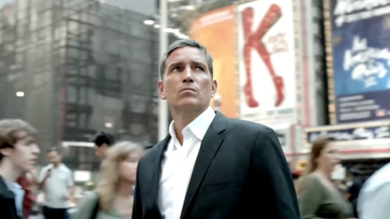 John Reese standing on a busy street and looking up