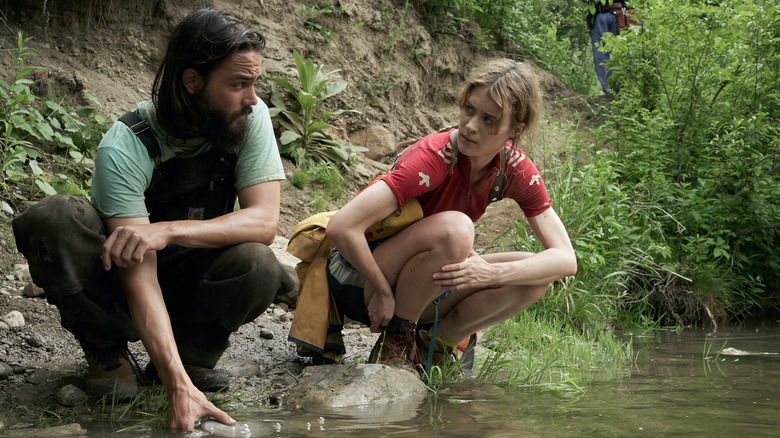 Tyler and Kirsten squatting in a creek talking on Station Eleven