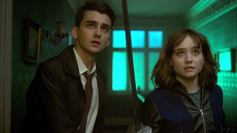 Anthony Lockwood (Cameron Chapman) and Lucy Carlyle (Ruby Stokes) look up while holding a sword in a green hallway in Lockwood & Co.