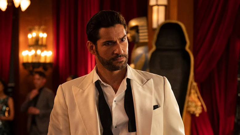Lucifer Morningstar (Tom Ellis) wears a white tuxedo with an undone bowtie in a fancy lounge in Lucifer
