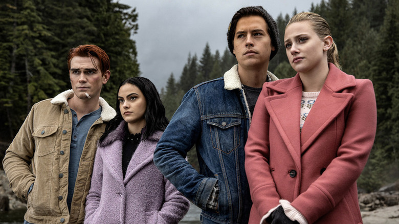 Archie Andrews (KJ Apa), Veronica Lodge (Camila Mendes), Jughead Jones (Cole Sprouse), and Betty Cooper (Lili Reinhart) look at the horizon in a forest in Riverdale