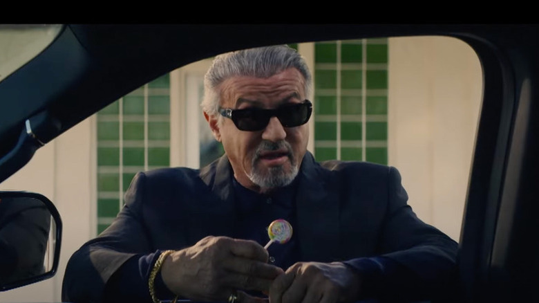 Dwight Manfredi (Sylvester Stallone) holds a lollipop while looking inside a car in Tulsa King